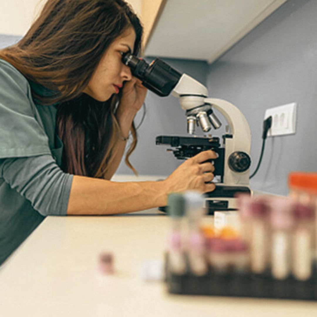 a person in a lab coat looking through a microscope